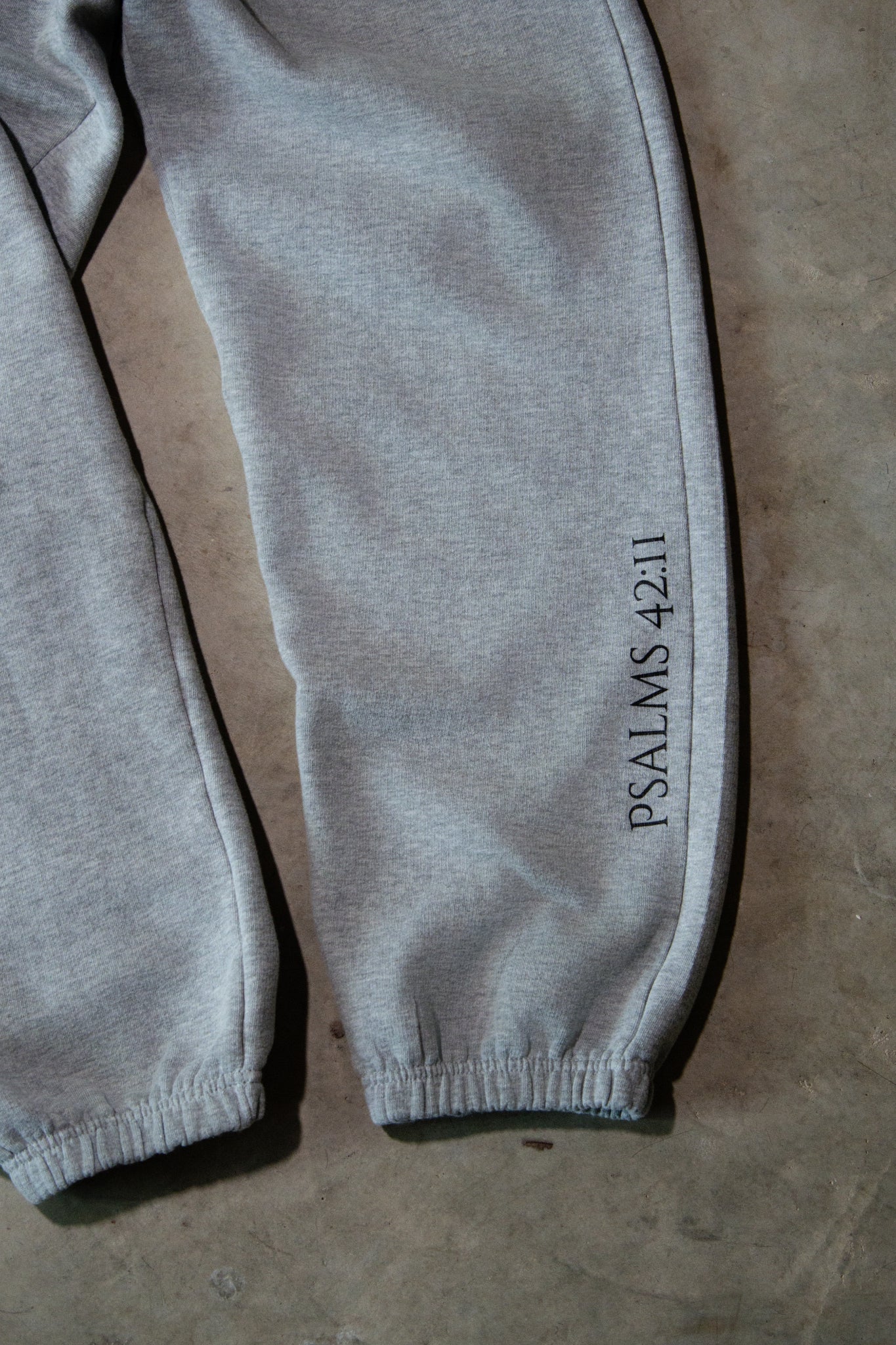 Gray sweatpants with 'PSALMS 42:11' text on a brown surface